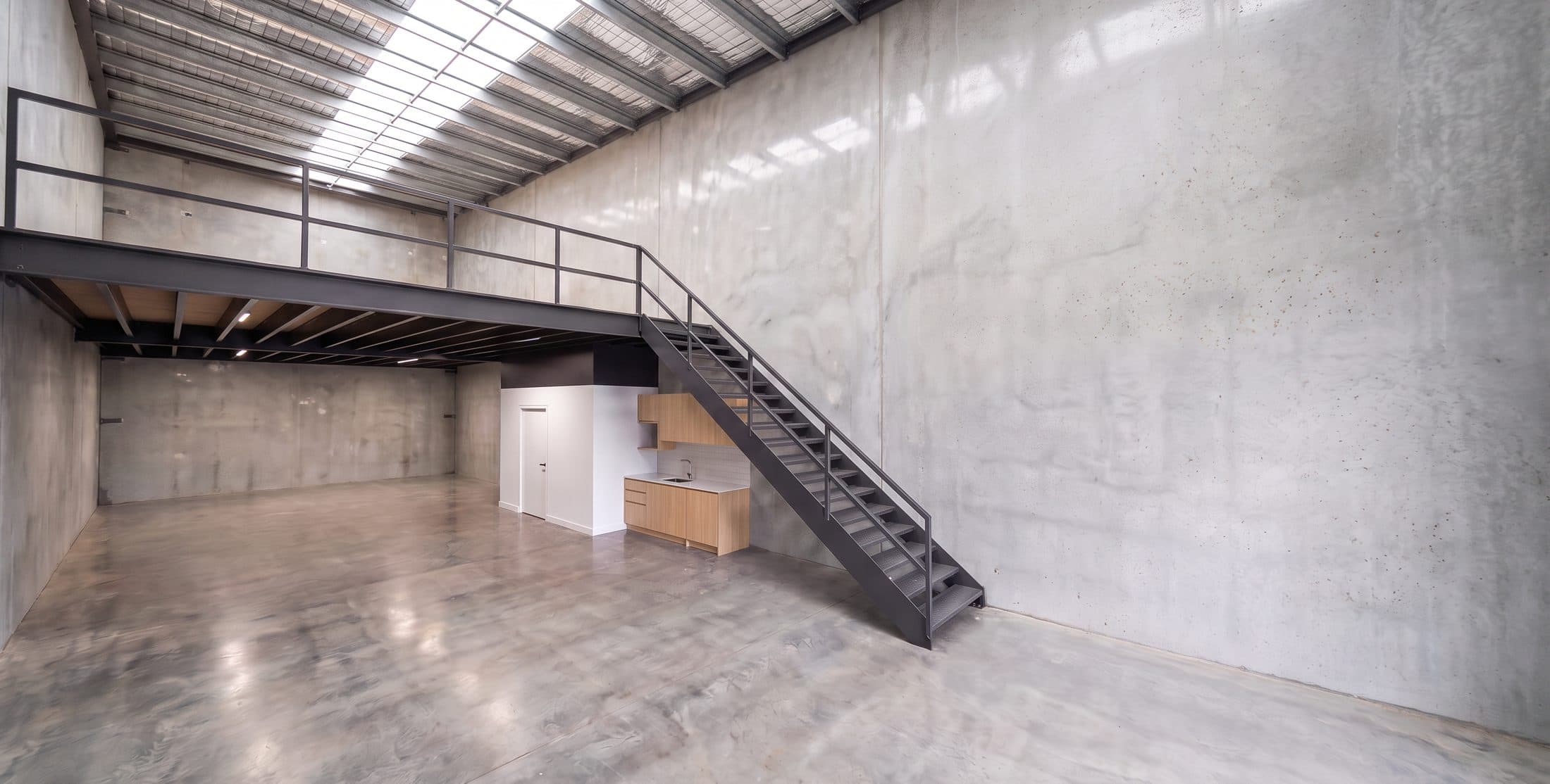 Bare warehouse interior at handover, showing the mezzanine and steel stair